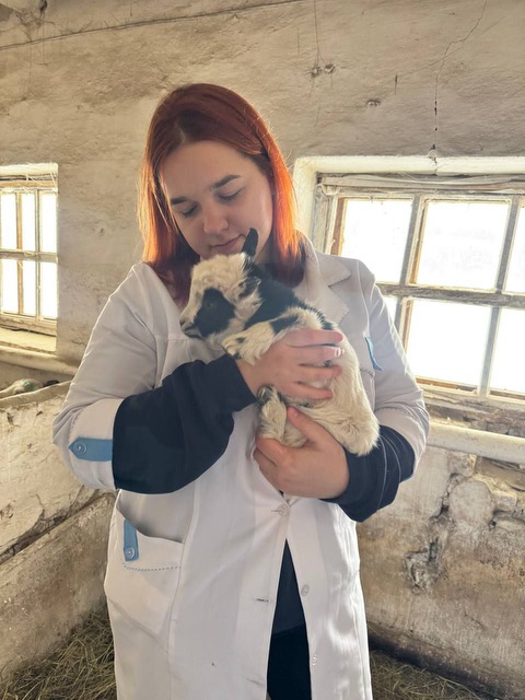 Dasha Pavlenko in her veterinary school lab coat, holding a lamb